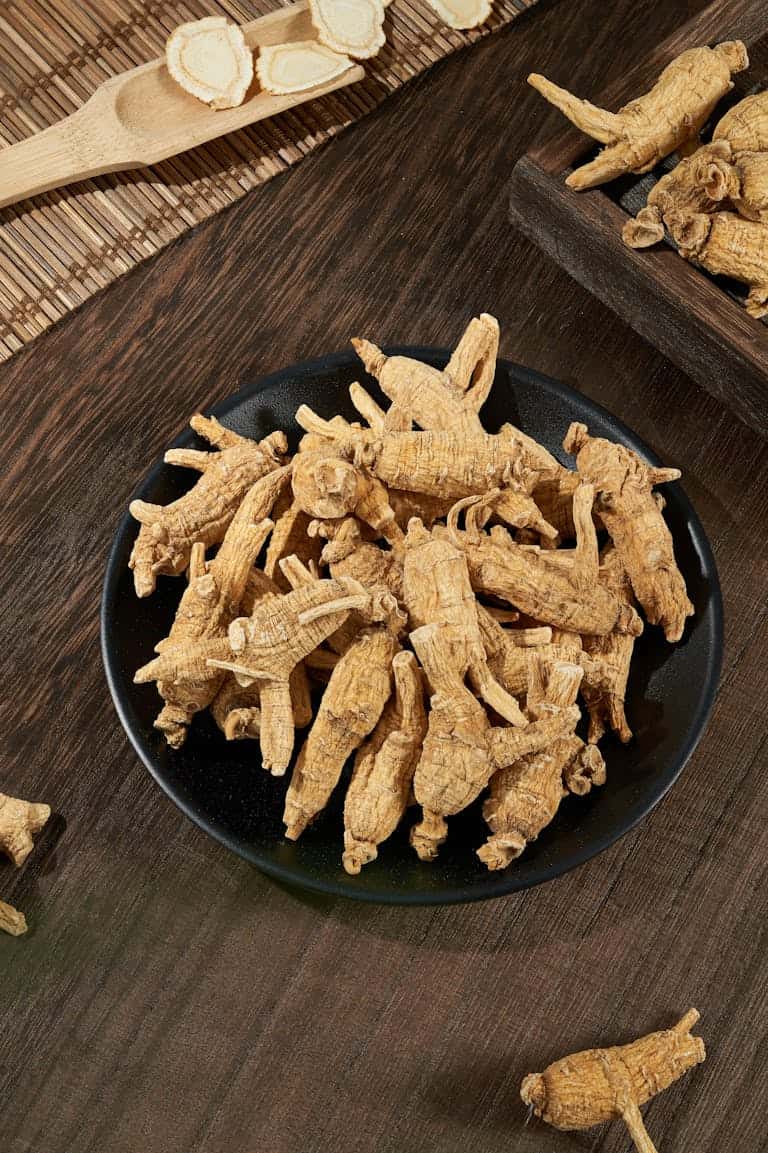 High angle view of fresh ginseng roots on a black plate on a wooden table, showcasing the natural texture and earthy tone.