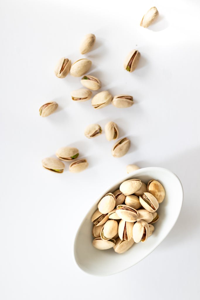 Pistachio nuts in a white bowl on a white background, top view.