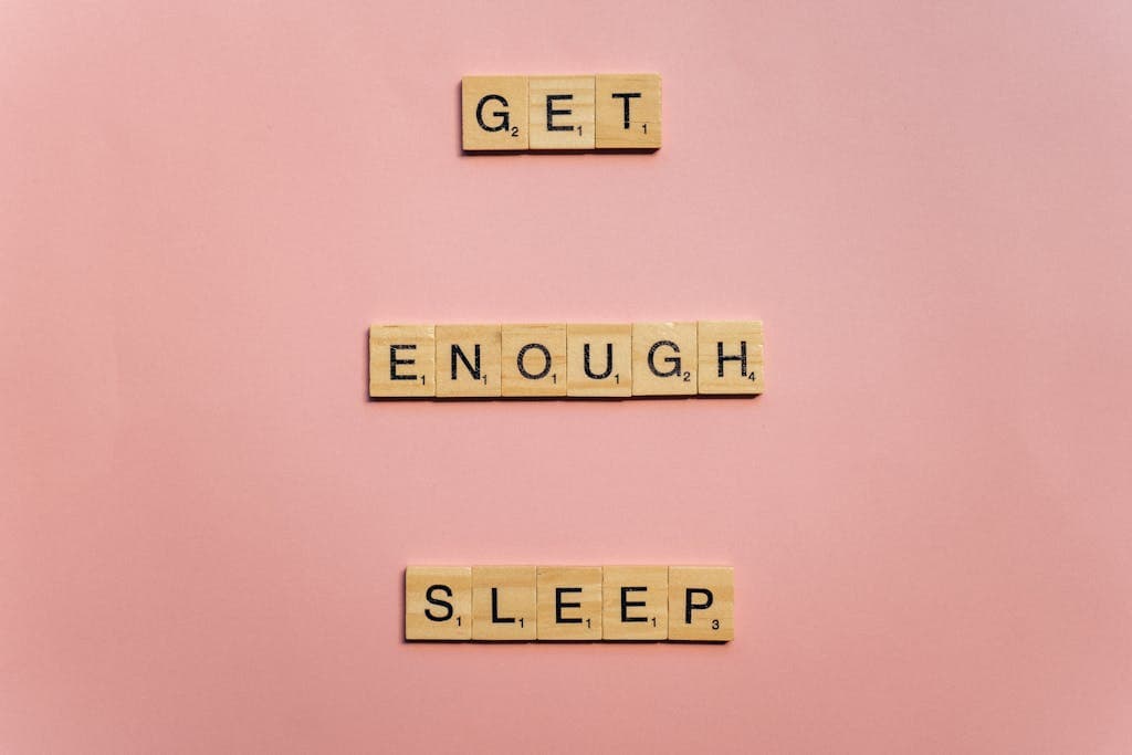 Scrabble tiles on a pink background spelling out 'Get Enough Sleep'. Ideal for wellness and lifestyle themes.