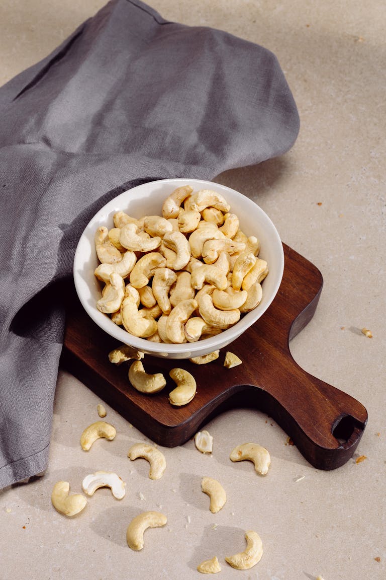 Top view of cashew nuts in a bowl on a wooden cutting board, perfect for healthy snack concepts.